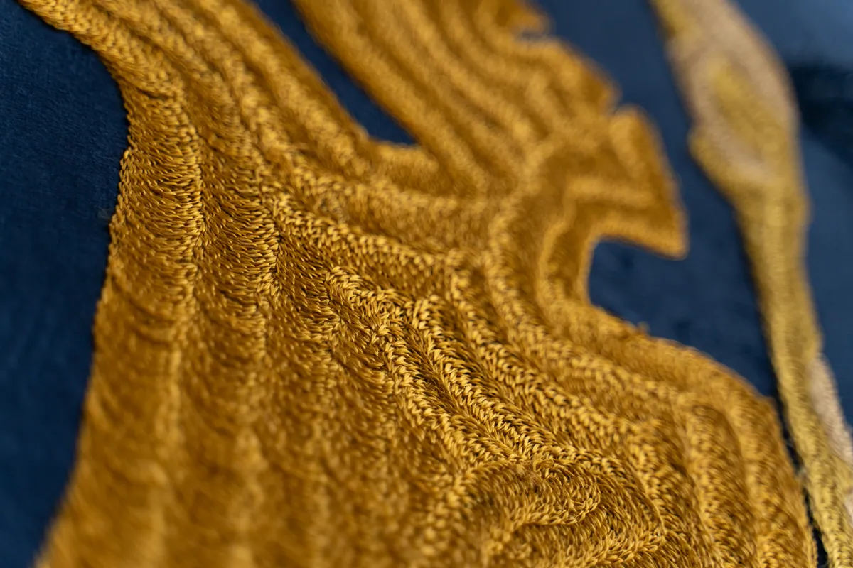 Macro detail of ridged gold cord embroidery against indigo cloth